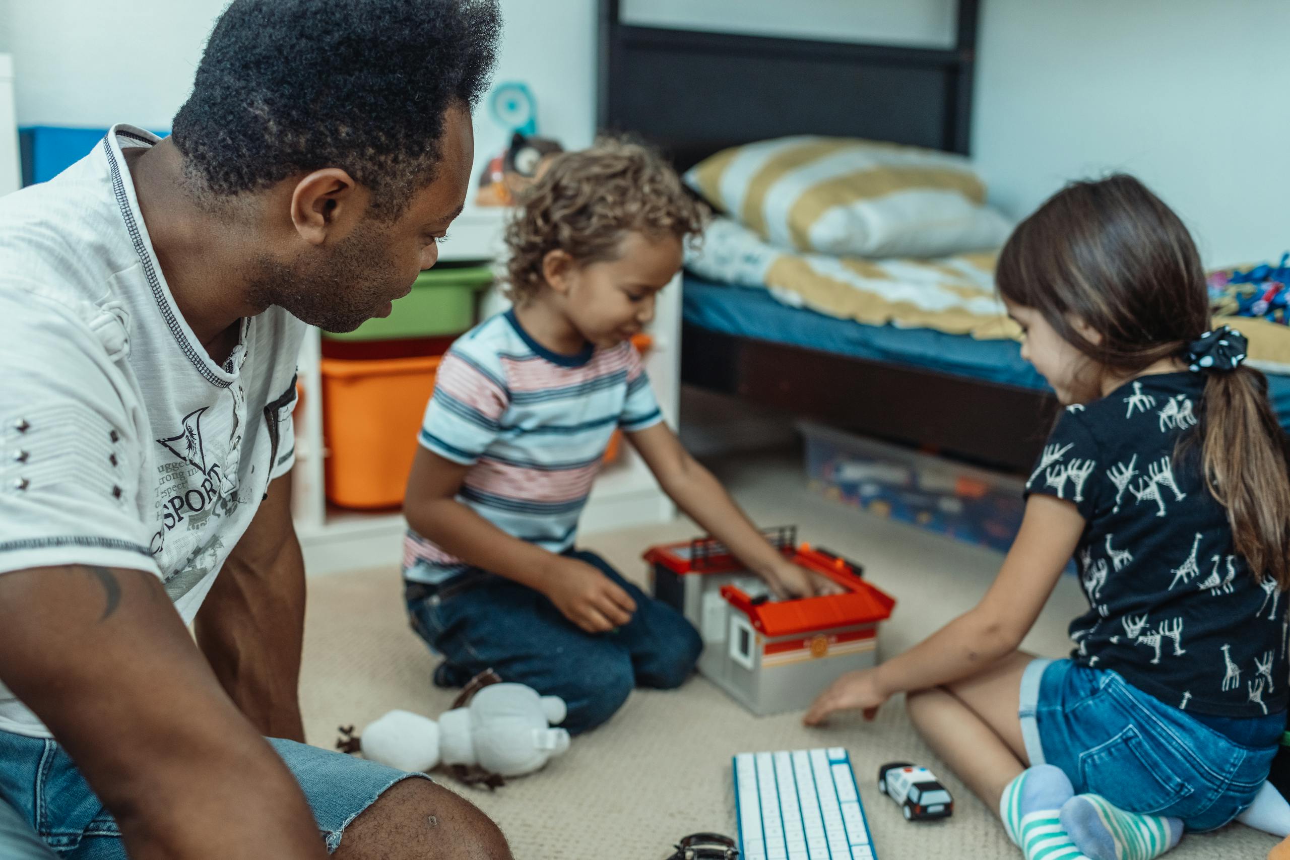 A father and two children enjoying playtime together in a cozy bedroom setting.