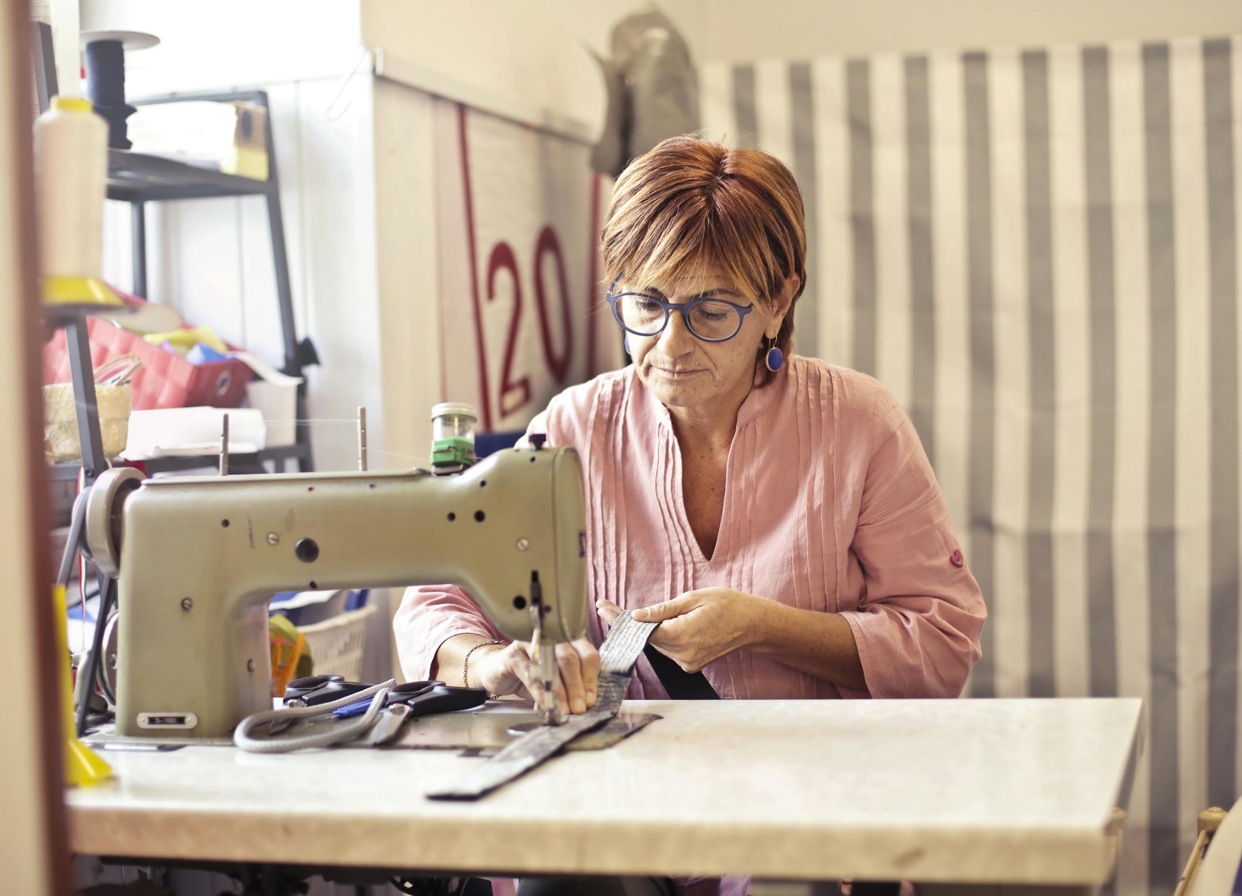 A woman intently working with a sewing machine in her workshop, showcasing craftsmanship.