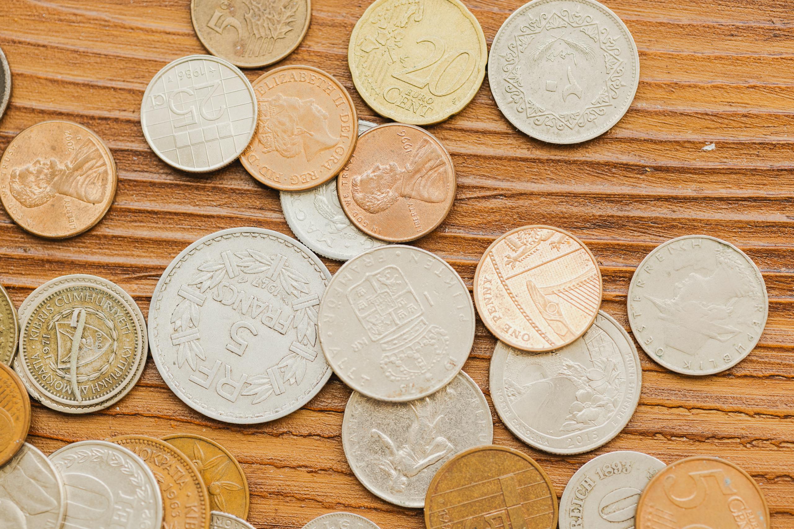 A collection of diverse vintage coins scattered on a wooden surface, showcasing international currency designs.
