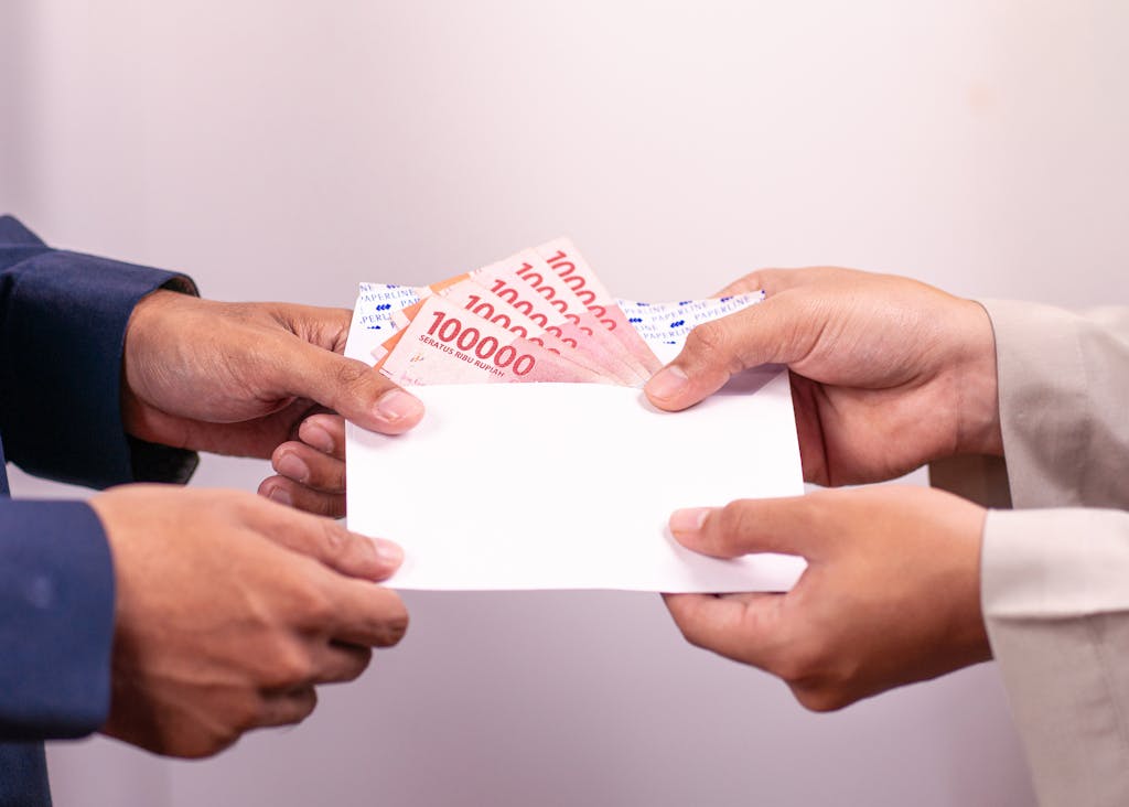 Hands exchanging an envelope with Indonesian Rupiah, highlighting financial transactions.