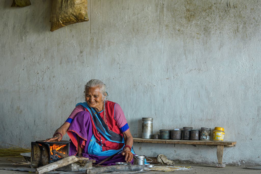 Senior Indian woman cooking with traditional fire in a rustic setting.